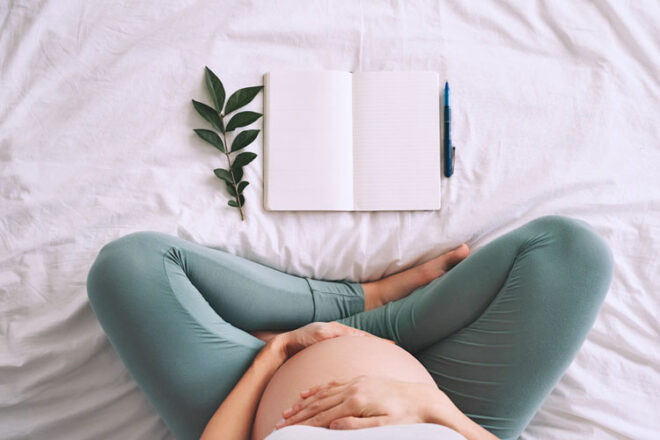 Pregnant woman sitting on a bed with a pregnancy journal