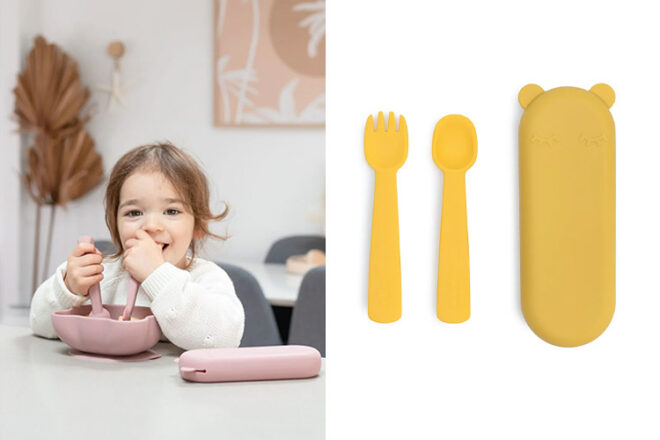 Smiling toddler using We might be tiny baby cutlery next to a spoon and fork with its matching cutlery case showing colours, size and fun design