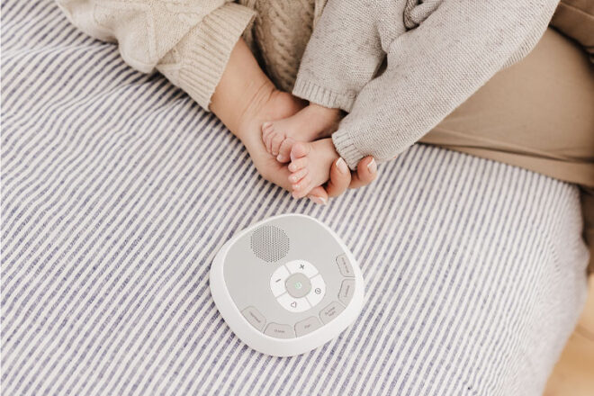 Mother and baby sitting on a bed with the Welcare Sleep Tight Sound Machine
