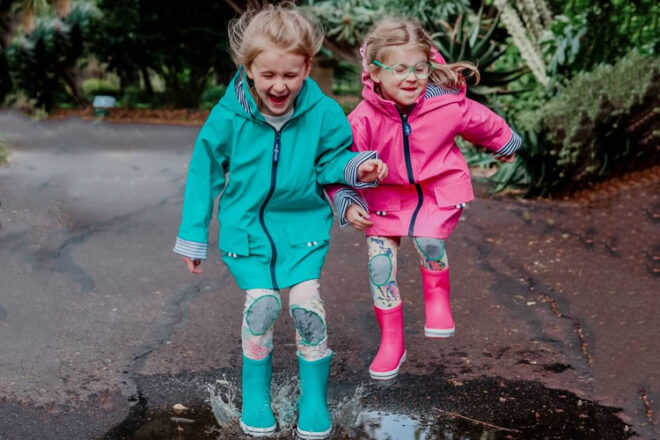 Two young girls jumping in puddles wearing French Soda Rain Jackets in Sea Green and Pink