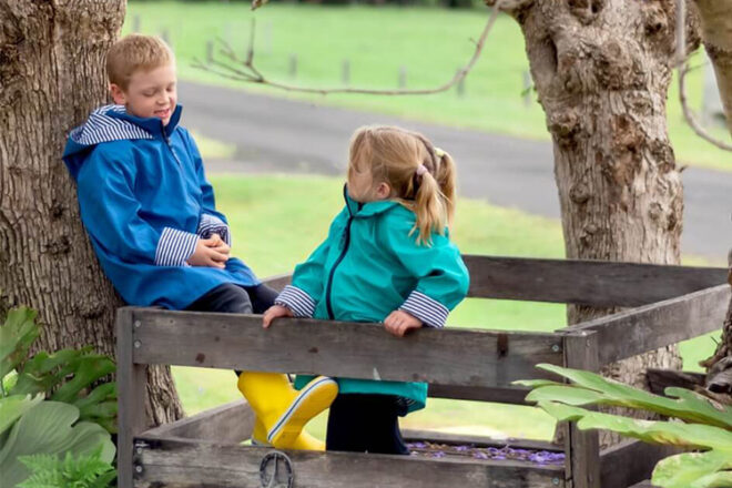 Two children in a tree house wearing French Soda green and blue kids raincoat showing outfit use and style