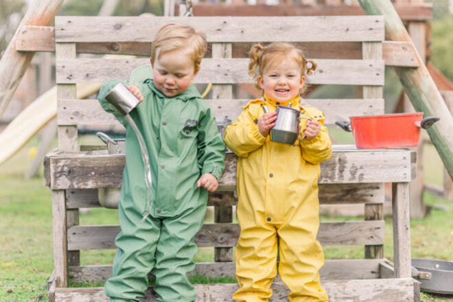 Two children wearing a Grubbybub Puddle Suit in Sunshine and Sage