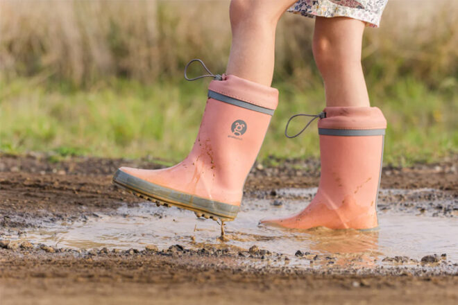 A child jumping in a muddy puddle wearing the Grubbybub Gumboots in Peach