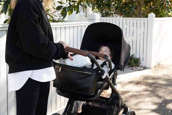 Nappy Society baby vegan pram caddy in black showing baby items securely stored on baby stroller whilst mum and baby are present 