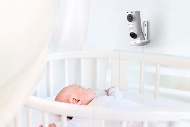 Baby sleeping in cot with the Oricom Dual Vision Camera mounted to the wall showing one camera on the baby and the other on the room