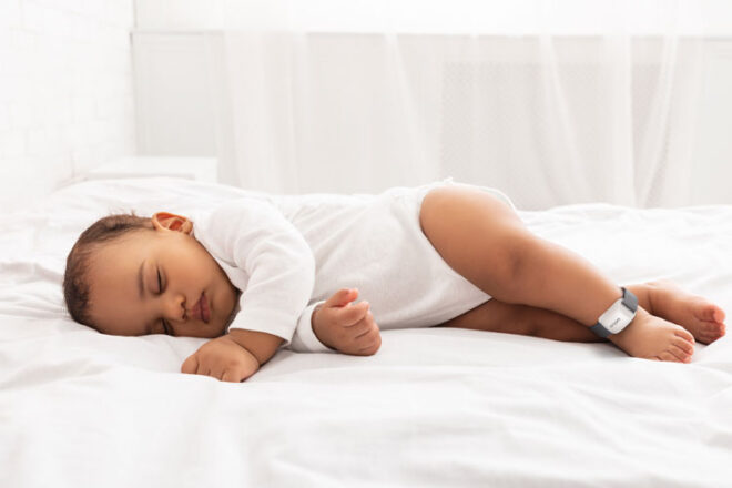 Baby laying on a bed wearing the Oricom Guardian Plus Wearable Sleep Tracker + Smart Soother