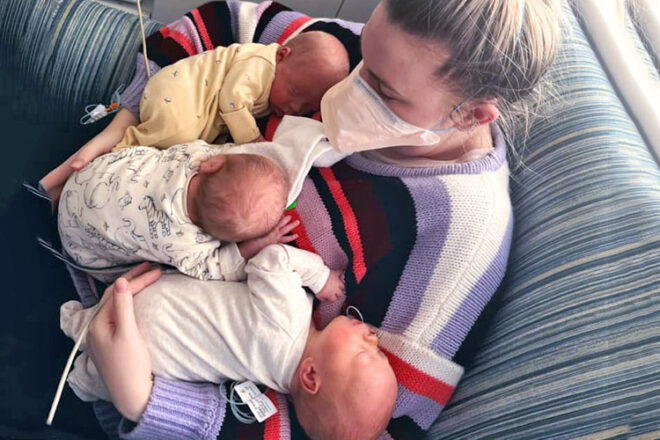Caitlin sitting on the couch holding her three triplet babies
