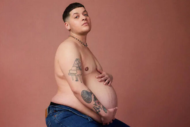 Logan Brown posing shirtless with his baby bump