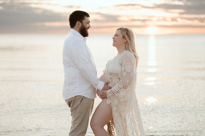 A couple stand on the beach pregnancy photo shoot