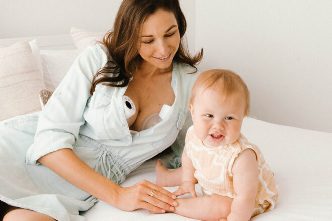 Mother and baby on a bed showing the mother wearing two wearable breast pumps discreetly