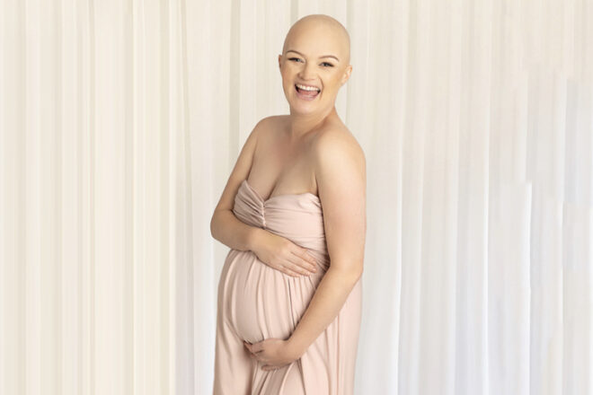 pregnant woman who suffers cancer with no hair holding belly