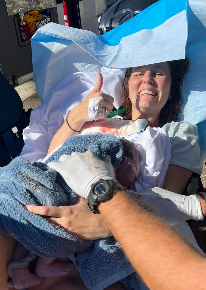 Blaize gives a thumbs up with her newborn baby on her chest
