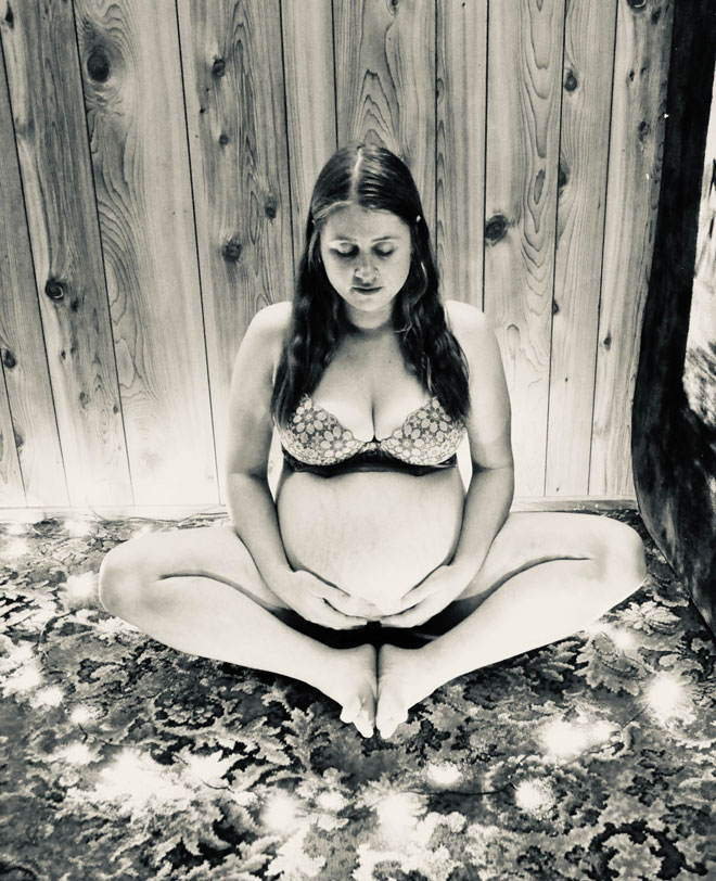 A pregnant Cassaundra sits on the ground in a yoga pose 