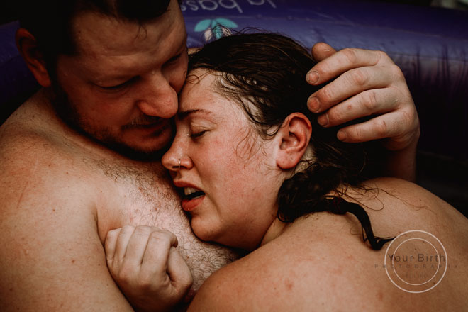 A close up of Cassaundra’s face being hugged by her husband in the birth pool
