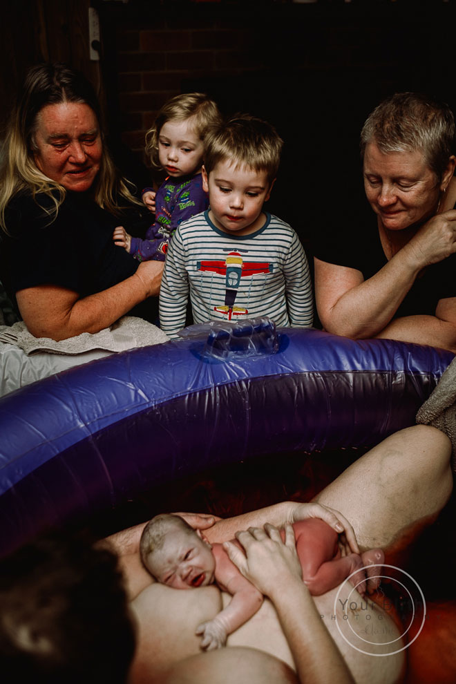 Siblings gather around the birth pool after the baby is born
