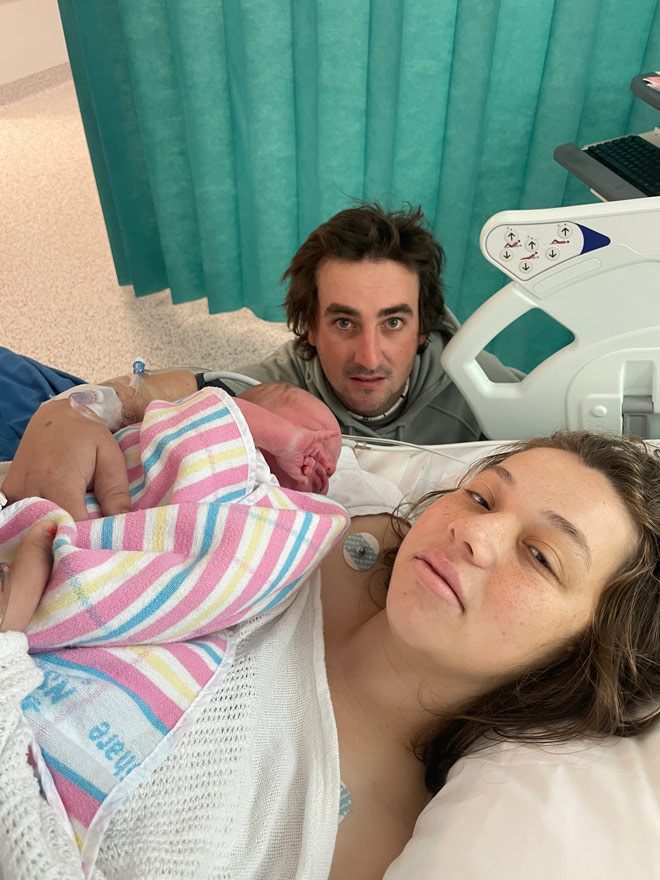 mother in hospital bed holding newborn with husband looking on