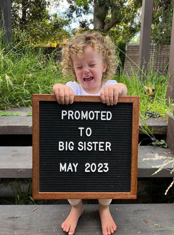 Lara's daughter holding sign to announce pregnancy