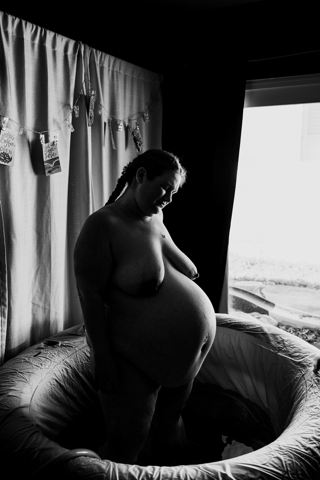 A black and white image of a pregnant woman standing in water