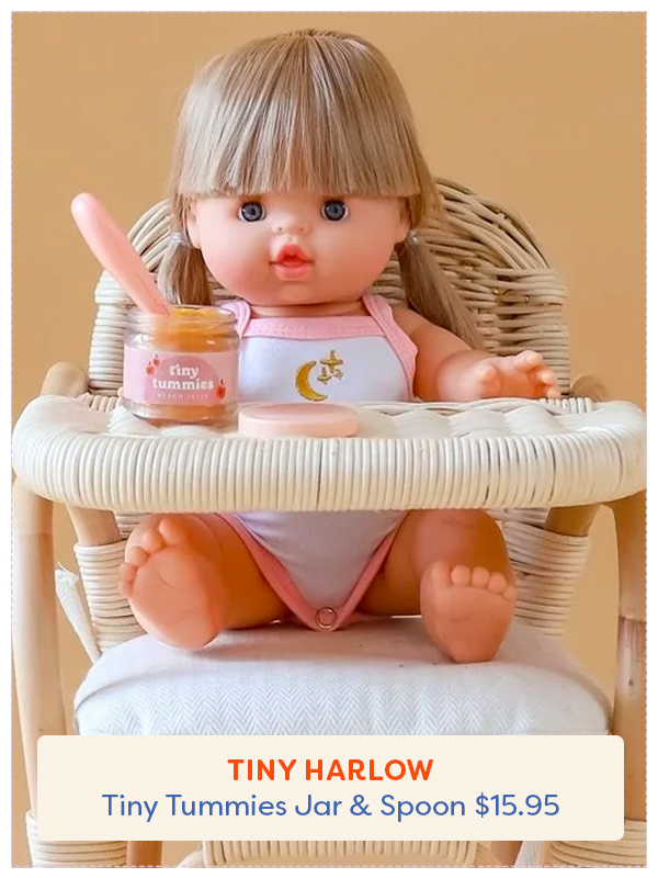 A baby doll sitting in a high chair with a jar of the Tiny Harlow custard and spoon