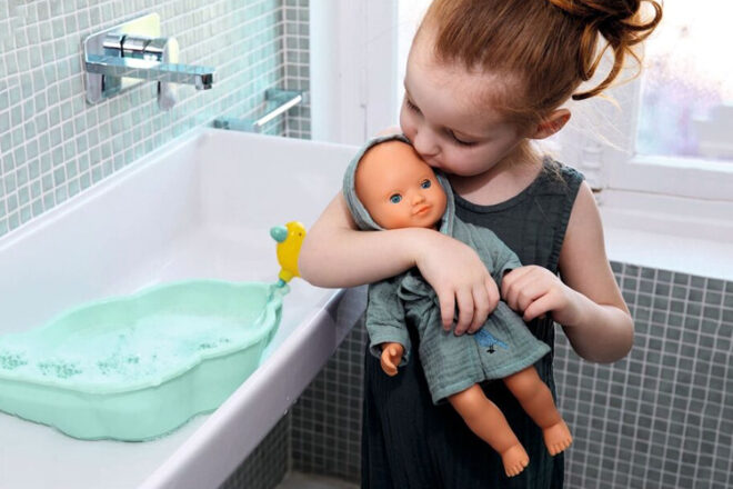 A young child holding and kissing their Djeco Baby Doll in the bathroom