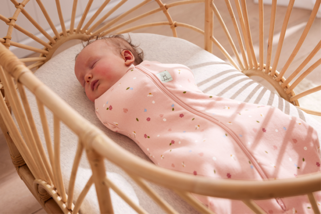 Baby sleeping in rattan bassinet in ergoPouch swaddle bag