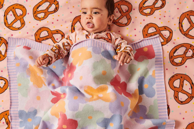 Baby lying in a cot with pretzel sheets and paper daisy cotton knit blanket from Kip&Co