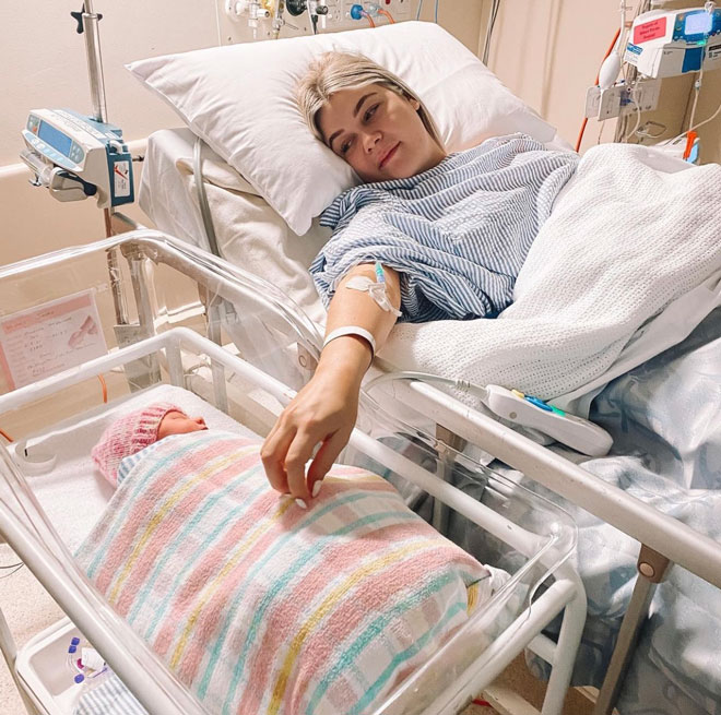 Mandy in a hospital bed reaches out to newborn in crib