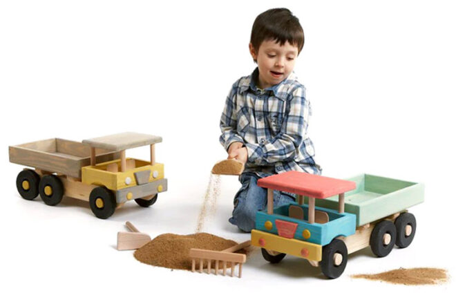 young boy playing with sand and large wooden toy trucks