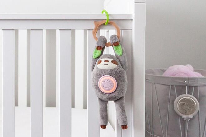 Santi the Sloth Sleep Aid hanging from a child's cot on a ring
