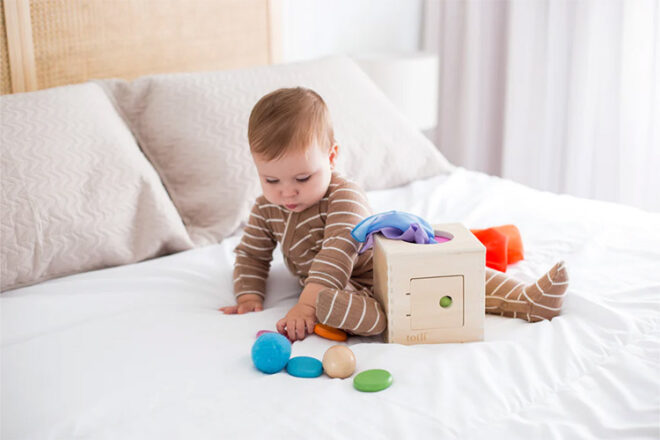 Totli box showing a baby sitting on a bed playing with the box and brightly coloured silks, coins and balls 