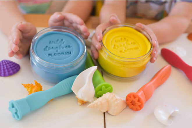 Image showing two pairs of hands holding a tub each of the Wild Dough playdough in blue and yellow surrounded by playdough accessory toys
