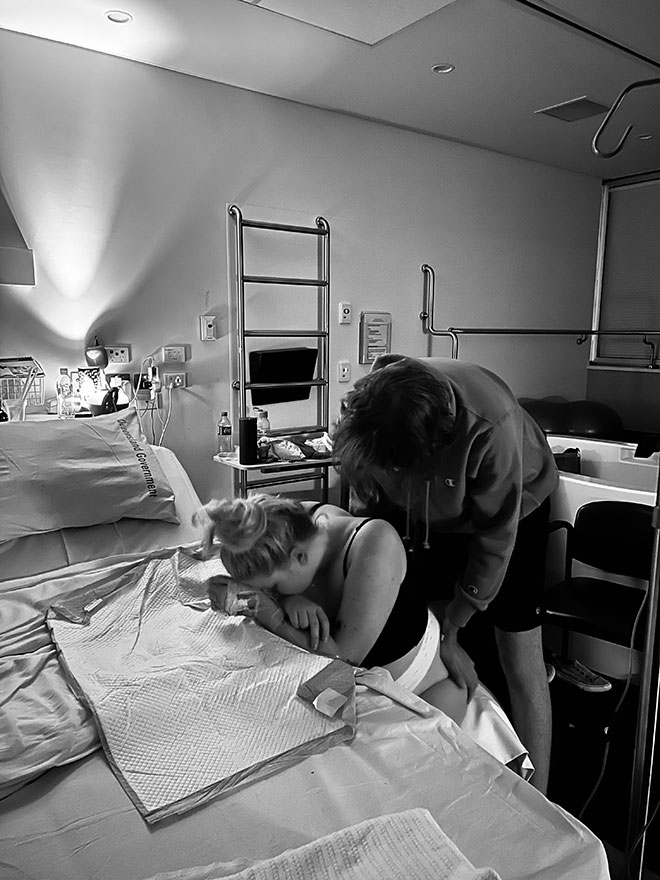 Birth partner helping mother through the contractions while she leans over the side of a bed.