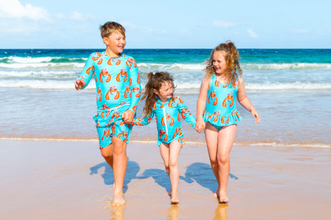 Three children wearing Cheeky Chickadee children's swimwear, showing matching styles and sizes for different age groups, and bright print.