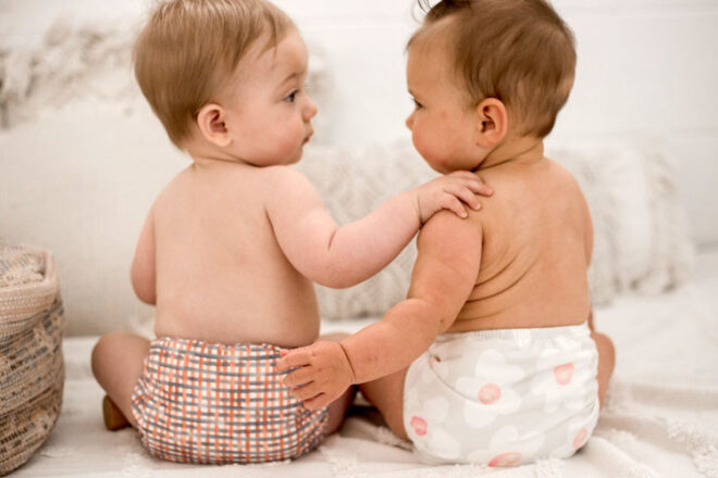 Two babies sitting next to one another wearing the My Little Gumnut cloth nappies
