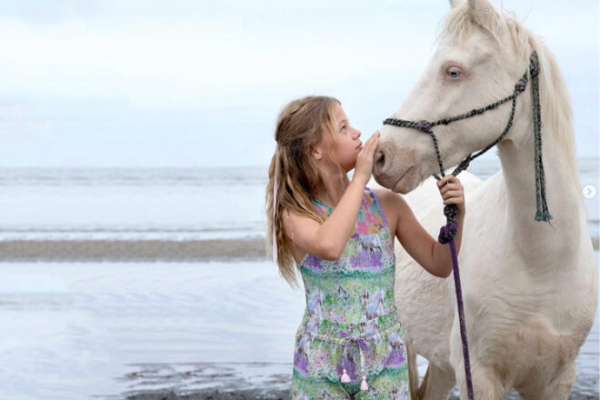 girl standing in water holding a white horse in Olga Valenting swimwear for kids