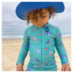 Young boy at the beach wearing Purebaby youth swimwear, showing the style and prints for girls and boys, plus matching hat.