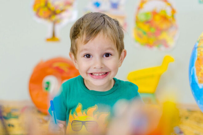 Young boy smiling at the camera surrounded by colourful artwork