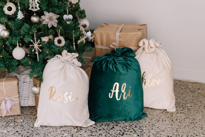 Three personalised velvet santa sacks sitting under a christmas tress