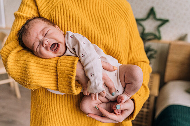 mother in a yellow jumper holding a crying baby in the football hold.