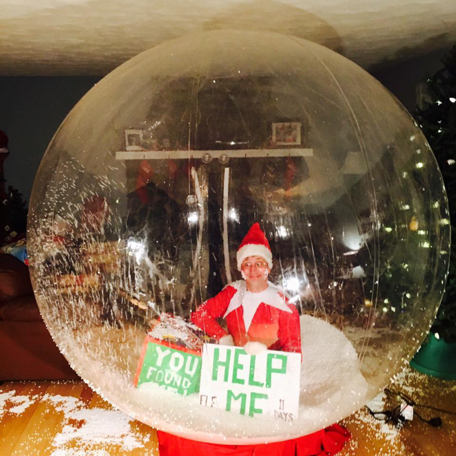 Dad dresses as elf on the shelf sitting inside a bubble representing a snow globe