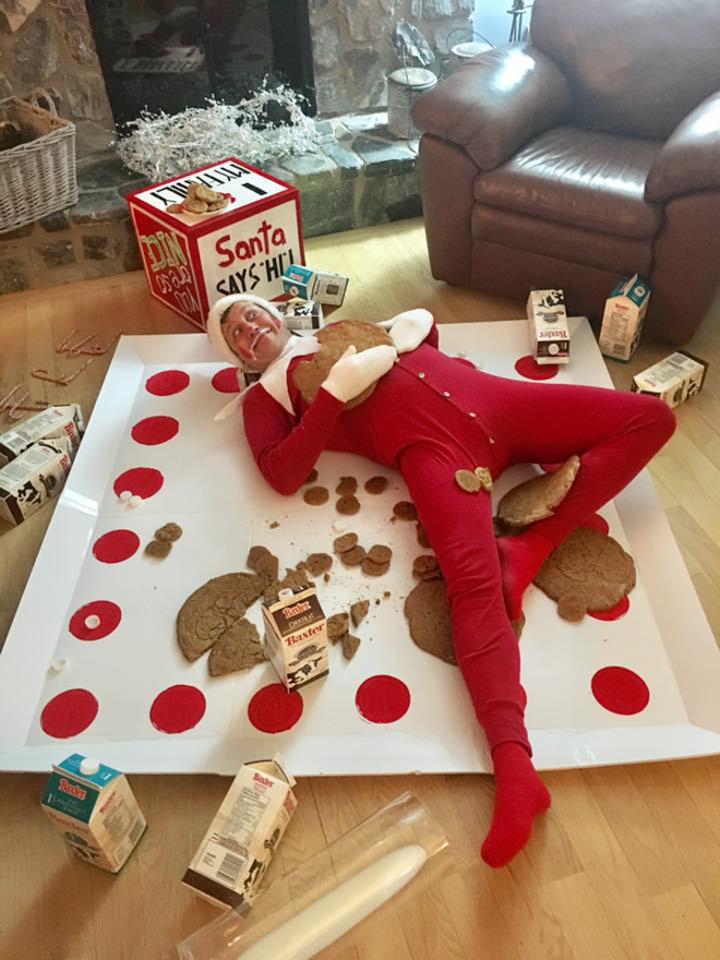 Dad dresses as elf on the shelf laying on overrides plate with milk and cookies