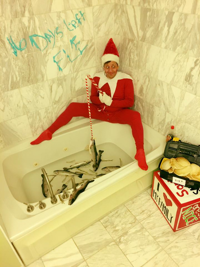 Dad dresses as elf on the shelf sitting on the edge of bath pretending to fish 