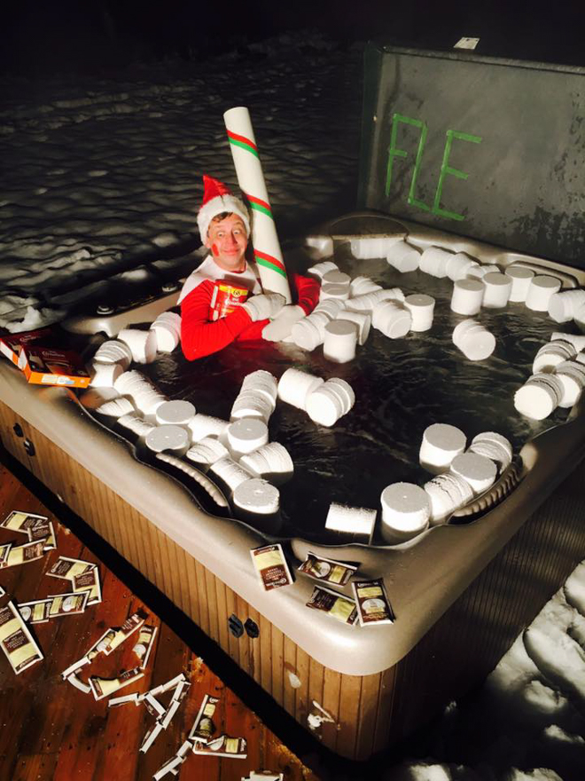 Dad dresses as elf on the shelf sitting in a hot tub with giant marshmallows to look like a giant hot chocolate 