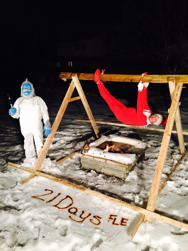 Dad dresses as elf on the shelf next to a yeti pretending to be a pig on a spit
