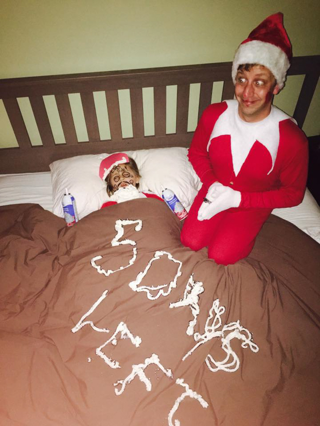 Dad dresses as elf on the shelf and sits next to sleeping child with whipped cream on their face