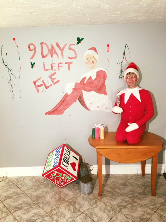 Dad dresses as elf on the shelf sitting next to a wall painting of himself