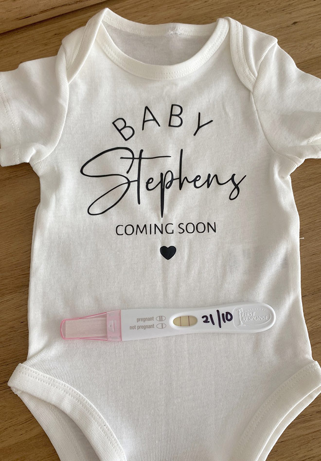 Onesie with coming soon on the front with a positive pregnancy test
