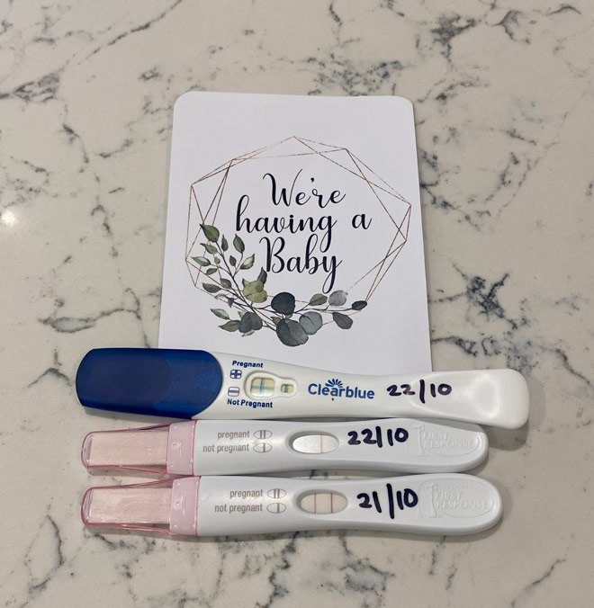 Three positive pregnancy tests with a milestone card saying 'We're having a baby'