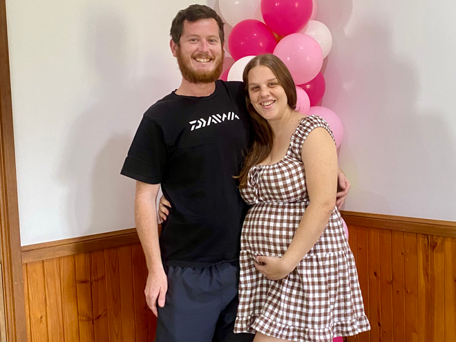 Andrew and pregnant Wandah standing under pink balloons
