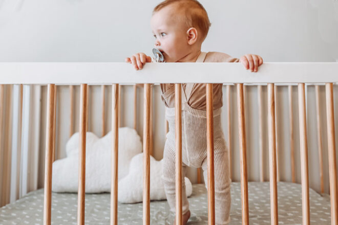 Baby standing in a cot with All4Ella cot sheets